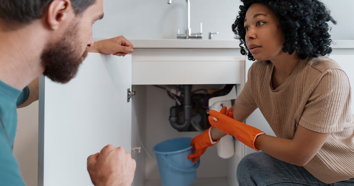 Woman holding a bucket under a leaky sink.