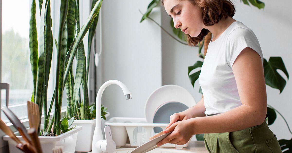 Woman in kitchen cleaning dishes in the sink. 