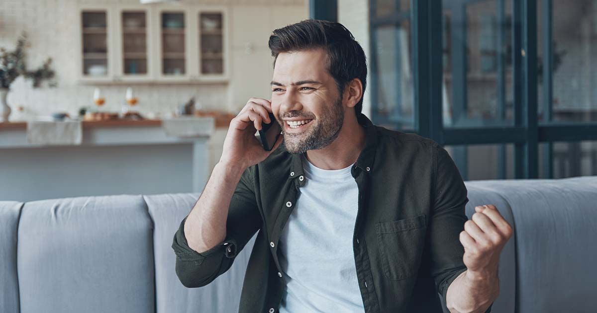 Man on the phone smiling, sitting on couch.