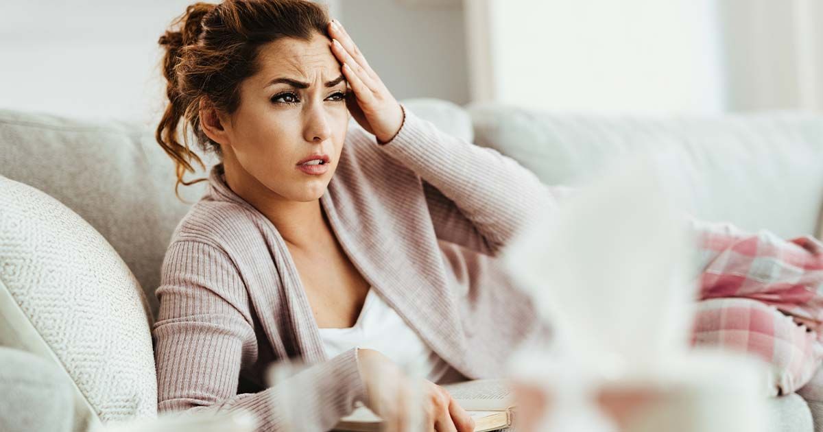 Woman laying on couch, in pain, touching head.