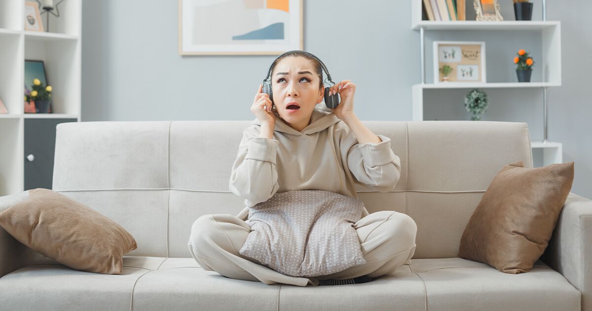 Woman sitting on couch looking concerned, taking her headphones off to hear a noise.