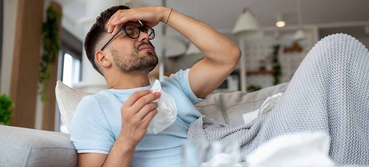 Man laying on couch, holding his head and tissues.