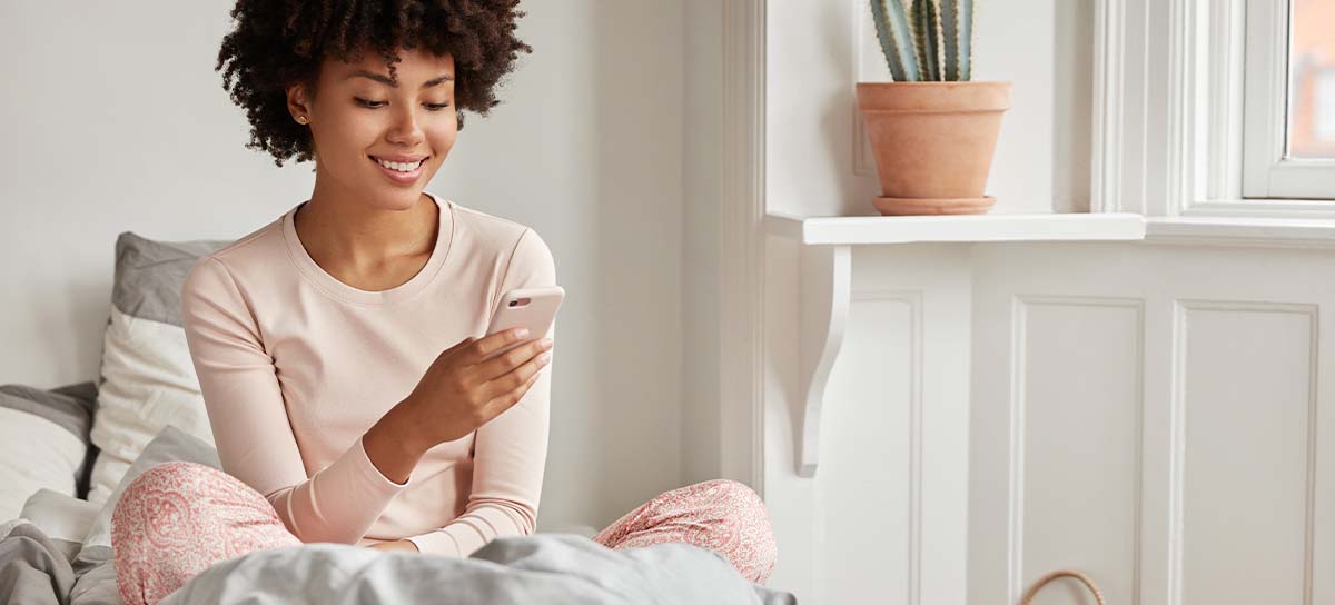 Woman sitting in bed looking at phone.